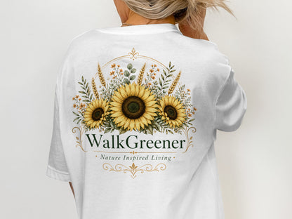 White t-shirt with a floral design featuring sunflowers, wheat stalks, and the text "WalkGreener Nature Inspired Living".