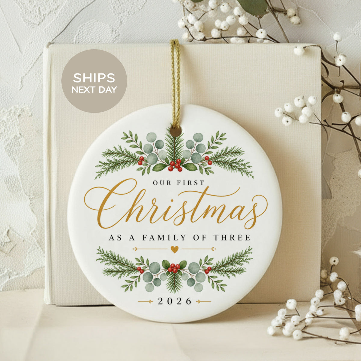 Round ceramic ornament reads "Our First Christmas As A Family of Three" and "2026".