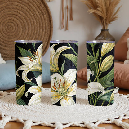 20oz stainless steel skinny tumbler with illustrated white lily flowers, cream petals and orange stamens, green leaves on a black background, clear straw lid, shown as a set of three
